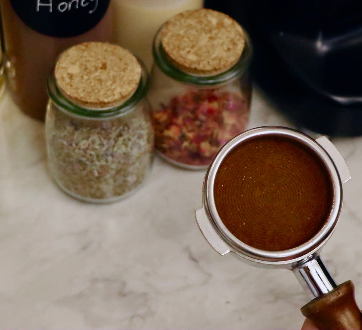 A freshly dosed portafilter beside jars of rose petals and dried herbs at Witches Brew Coffee Co.