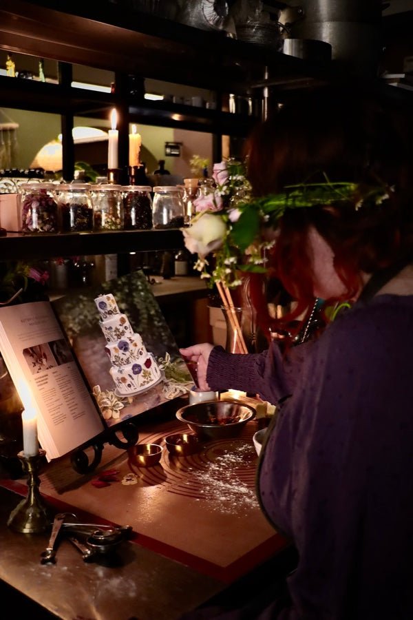 A candlelit bake counter at Witches Brew Coffee Co., with an open recipe book and gathered herbs
