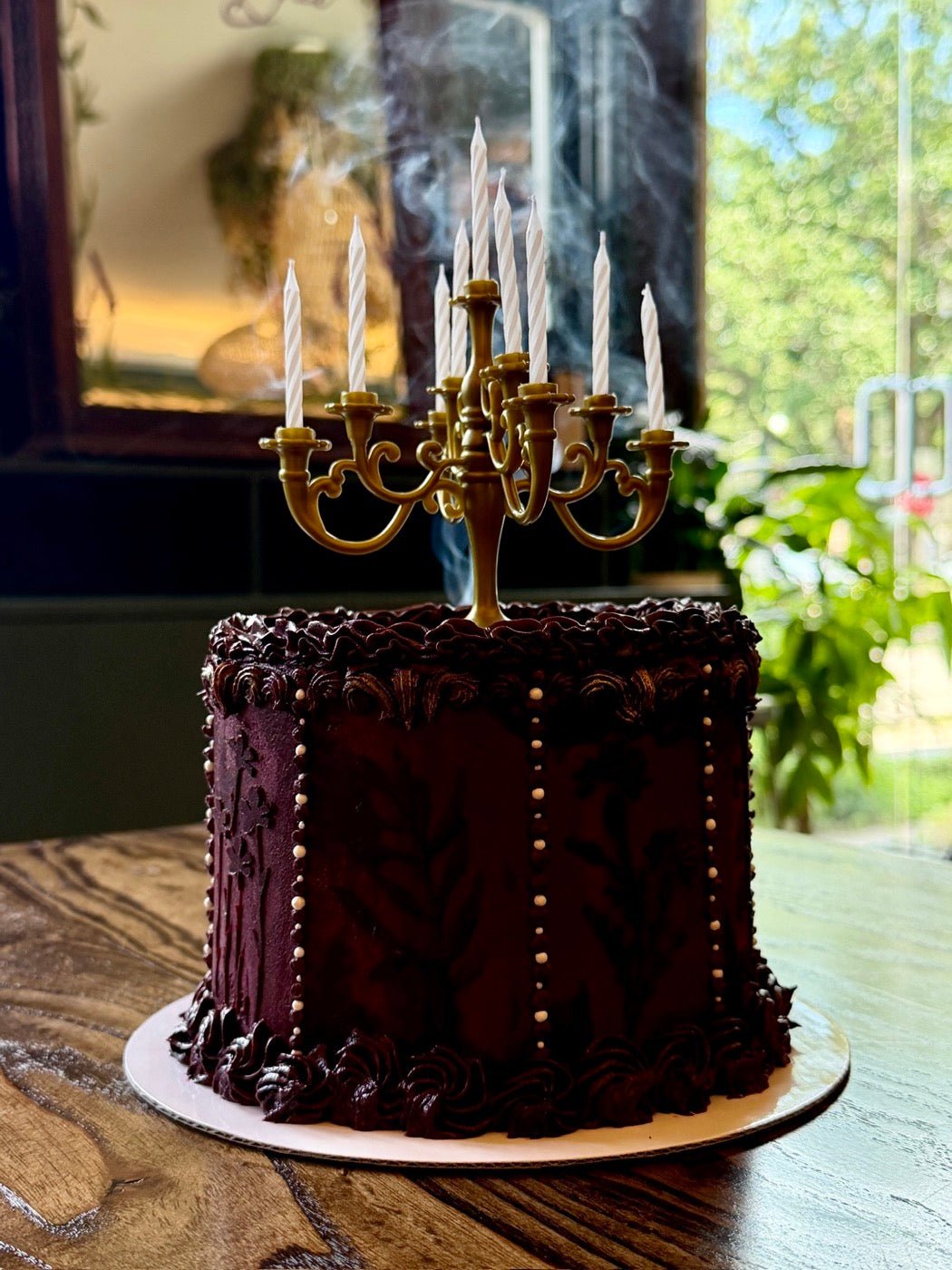 A deep burgundy custom cake with piped damask panels, crowned with a gold candelabra of lit candles