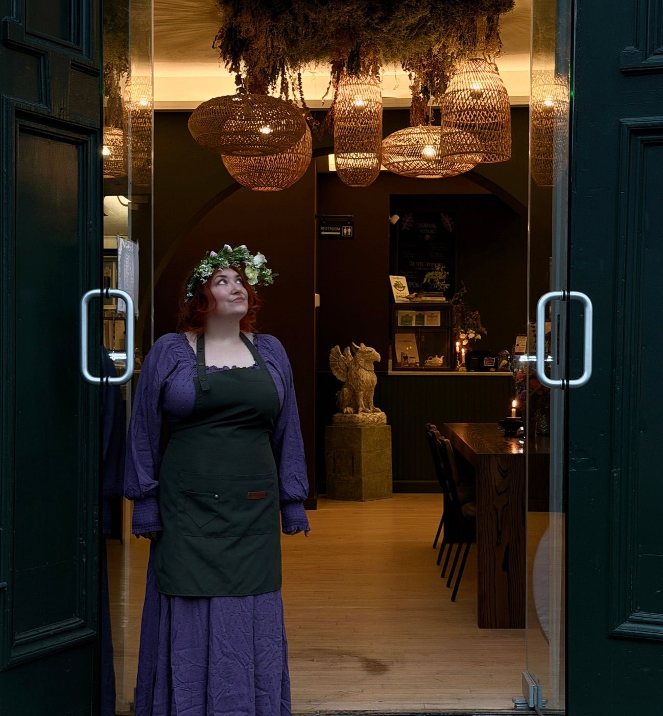 The doorway of Witches Brew Coffee Co. under woven lanterns and hanging moss, with Godwin the griffin on his pedestal inside